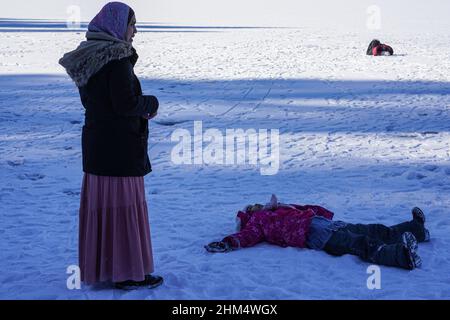 Une touriste asiatique avec foulard se trouve sur la surface de glace d'Eibsee, Zugspitze. Son enfant s'est posé sur le sol dans la neige. Banque D'Images