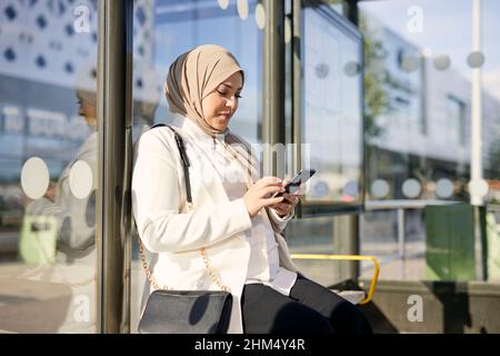 Femme utilisant un téléphone cellulaire à l'arrêt de bus Banque D'Images