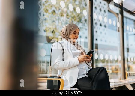 Femme utilisant un téléphone cellulaire à l'arrêt de bus Banque D'Images