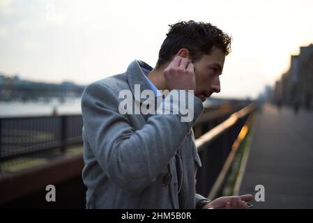 homme d'affaires à l'aube dans la ville mettant des écouteurs dans son oreille Banque D'Images