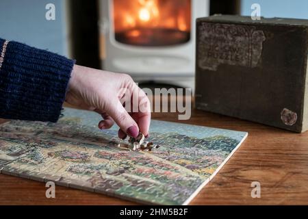 Une femme est assise à côté d'un poêle à bois comme elle pièces ensemble une victoire vintage artistique 1930s puzzle en bois Banque D'Images