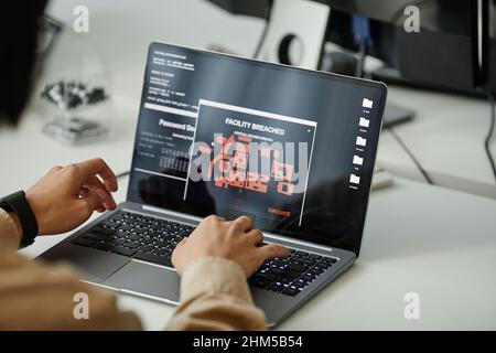 Mains d'un programmeur contemporain appuyant sur les touches du clavier d'ordinateur portable tout en étant assis sur le bureau et en travaillant avec des données décodées Banque D'Images