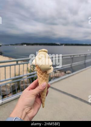 Main de femme tenant une glace douce savoureuse dans un cornet de gaufres avec la mer sur fond Banque D'Images