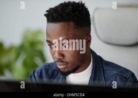 Jeune travailleur de bureau afro-américain sérieux regardant l'écran d'ordinateur pendant la communication en ligne ou de travailler avec des données Banque D'Images