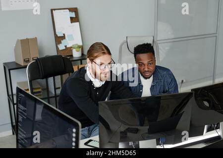 Jeune barbu en lunettes et son collègue afro-américain regardant l'écran d'ordinateur à la réunion de travail Banque D'Images
