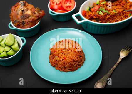 Jollof riz sur une assiette. Riz aux tomates, oignons, épices. Nourriture traditionnelle nationale nigériane. Arrière-plan sombre. Banque D'Images