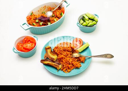 Riz Jollof avec banane frite sur une assiette. Riz aux tomates, oignons, épices. Légumes frais. Arrière-plan blanc. Banque D'Images