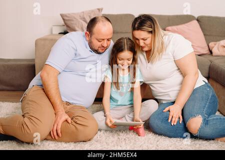 Mère et Père avec leur fille entre eux assis ensemble sur le tapis à la maison, passant une belle journée dans la famille. Banque D'Images