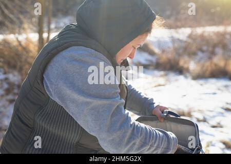 Vue latérale photo d'une femme voyageur dans des vêtements chauds dehors le jour ensoleillé de neige ouvrir son sac et à la recherche de quelque chose. Banque D'Images