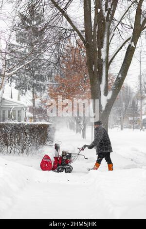 Homme nettoyant une allée couverte de neige avec une souffleuse à neige. London, Ontario. Canada Banque D'Images