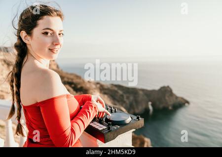 Les femmes du DJ jouent de la musique en mélangeant et en grattant le soir avec fond de mer et doux coucher de soleil chaud.Gros plan d'une console DJ contrôlée par Banque D'Images