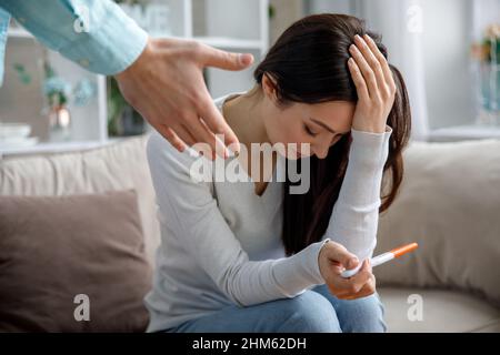 Une jeune femme triste tient un test de grossesse dans sa main. Le concept de grossesse non désirée. Banque D'Images