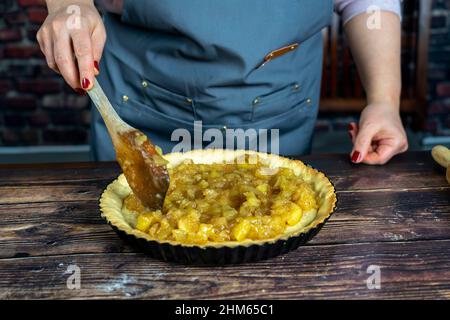 Femmes préparant une tarte aux pommes délicieuse ou une grande tarte sur fond de table en bois.Spredding la pomme confite cuite sur la pâte Banque D'Images