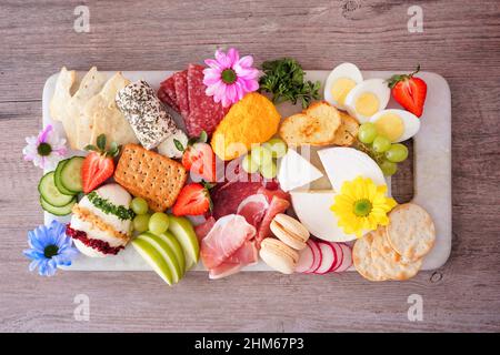 Charcuterie à thème printemps ou Pâques sur fond de bois.Variété de fromages, viandes, fruits et légumes hors-d'œuvre.Vue de dessus. Banque D'Images