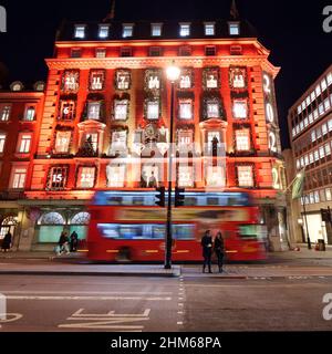 Londres, Grand Londres, Angleterre, janvier 4th 2022 : le bus passe par Fortnum et Mason Shop avec sa façade illuminée de Noël la nuit sur Piccadilly. Banque D'Images