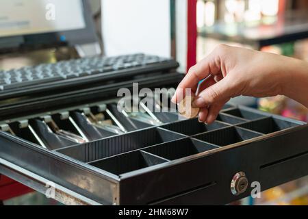 latina fille prenant l'argent de la caisse, de retour d'argent dans son magasin d'alimentation, fille prenant un millier de peso colombie pièce avec sa main. con Banque D'Images