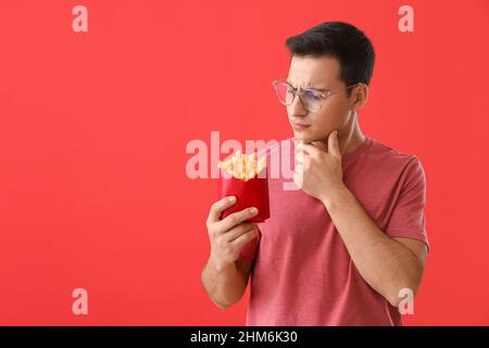 Jeune homme attentionné avec frites sur fond rouge Banque D'Images