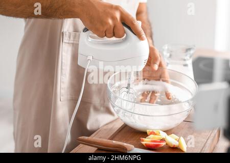 Jeune homme fouetter l'œuf d'albumine avec le mélangeur tout en suivant la vidéo de cuisine tutoriel en cuisine, gros plan Banque D'Images