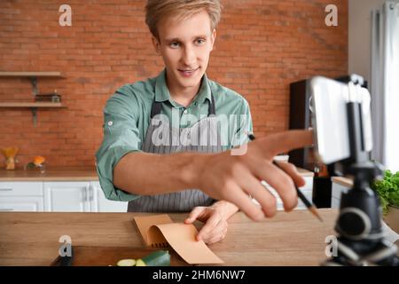 Jeune homme avec un ordinateur portable utilisant un téléphone portable dans la cuisine Banque D'Images