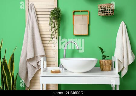 Table avec évier blanc, plantes de maison et savon près du mur vert dans la salle de bains Banque D'Images