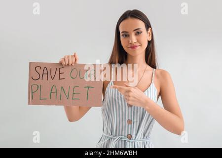 Jeune femme pointant sur du papier de carton avec texte SAUVER LA PLANÈTE sur fond clair Banque D'Images