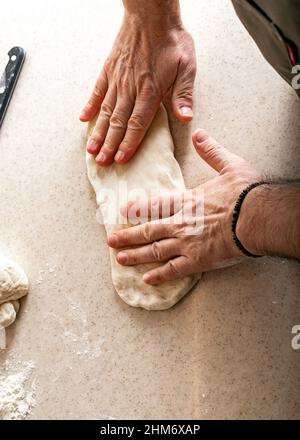 Les mains de sexe masculin pétrir la pâte. Mains humaines préparant la pâte pour la baguette maison. Tir vertical Banque D'Images