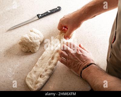 Les mains de sexe masculin pétrir la pâte. Mains humaines préparant la pâte pour la baguette maison. Banque D'Images