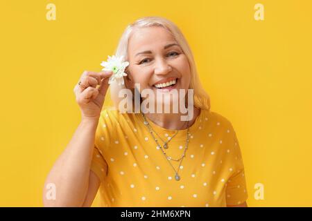 Bonne femme mûre tenant la fleur sur fond jaune. Célébration de la Journée internationale de la femme Banque D'Images