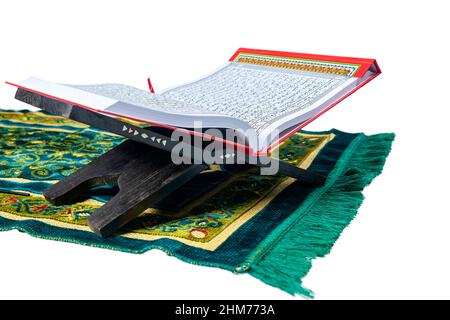 Quran ouvert sur un platemat en bois dans un tapis de prière isolé sur fond blanc Banque D'Images