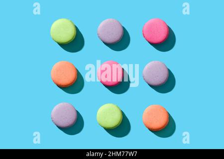 Macarons ou macarons de couleur pastel alignés dans un motif répétitif sur fond bleu vif. Banque D'Images