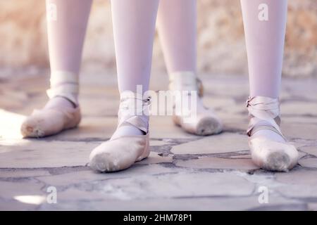 Pieds de deux ballerines debout dans une rangée sur un sol en pierre lors d'une répétition extérieure. Banque D'Images