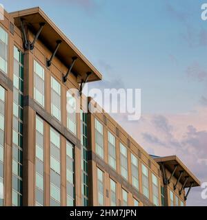 Carré nuages Puffy au coucher du soleil façade d'un bâtiment avec verre et de couleur Havane mur extérieur à Banque D'Images