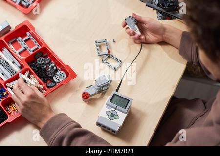 Vue de haut en bas chez un jeune homme méconnaissable qui assemble une voiture électrique en appréciant pendant un cours de robotique à l'école, espace de copie Banque D'Images