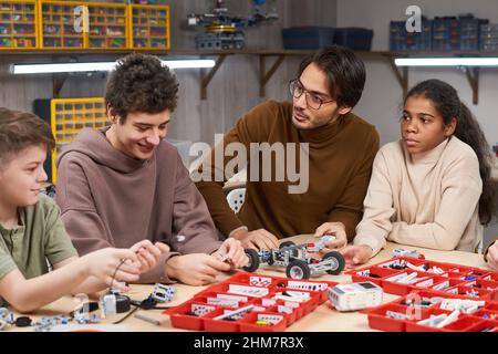 Portrait d'un jeune enseignant de sexe masculin aidant divers groupes d'enfants à construire des robots en classe d'ingénierie à l'école Banque D'Images