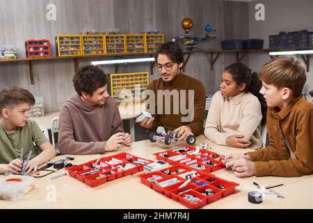 Portrait d'un enseignant souriant aidant un groupe diversifié d'adolescents à construire des robots en cours de robotique et d'ingénierie à l'école Banque D'Images