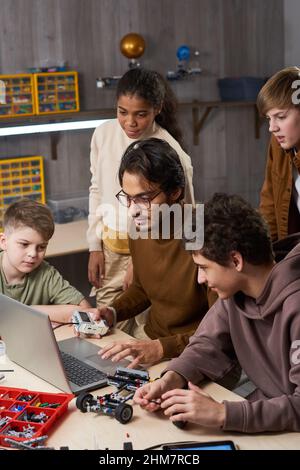 Portrait vertical de jeunes enseignants de sexe masculin avec divers groupes d'enfants en cours de robotique à l'école Banque D'Images