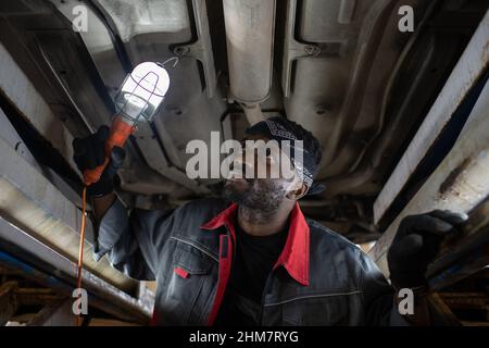 Portrait d'un mécanicien noir barbu inspectant la voiture sur un ascenseur dans un atelier de réparation automobile, espace de copie Banque D'Images