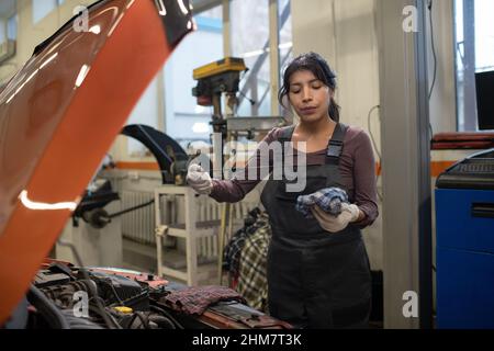 Portrait à la taille haute d'une jeune femme mécanicien vérifiant le niveau d'huile avec la jauge lors de la réparation de la voiture en atelier, copier l'espace Banque D'Images