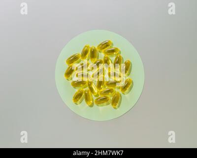Capsules liquides de vitamine D3 ou d'Omega ou d'huile de Primrose du soir sur un cercle vert sur fond gris neutre. Vue de dessus ou plat concept minimaliste avec capsules d'huile jaune liquide Banque D'Images
