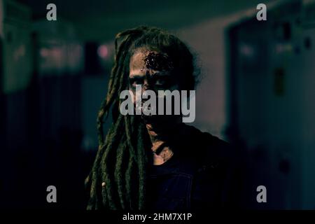 Vue de face d'une jeune femme portant un maquillage zombie FX et regardant l'appareil photo dans une pièce sombre, espace de copie Banque D'Images
