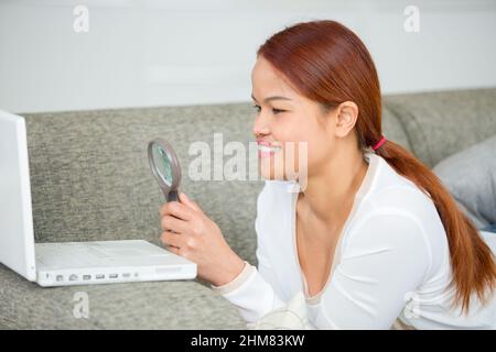 belle femme regardant à travers la loupe sur son ordinateur portable Banque D'Images