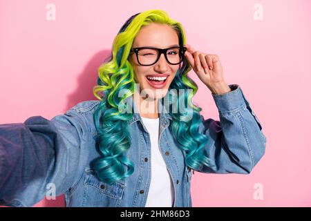 Photo de drôle mignon jeune dynamique femme porter Jean chemise bras lunettes wencing enregistrement vidéo sourire isolé couleur rose fond. Banque D'Images