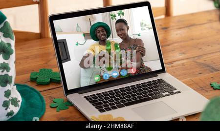 Webcam vue d'un couple afro-américain toaster des bières sur appel vidéo sur ordinateur portable sur table en bois Banque D'Images