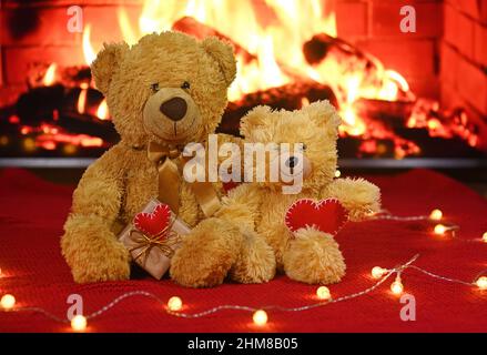 une paire d'ours en peluche est assise sur le fond d'un tissu tricoté rouge et d'une guirlande d'ampoules et tient deux coeurs rouges dans leur Banque D'Images