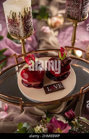Gâteau en forme de coeur avec glaçage à la gelée de fruits, rose et macarons sur le dessus comme décoration. Banque D'Images