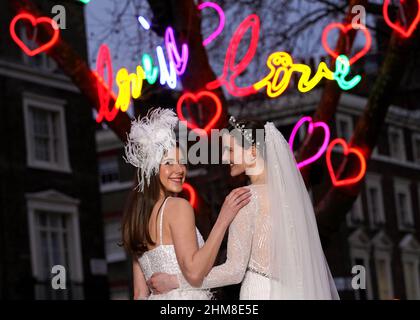 À USAGE ÉDITORIAL EXCLUSIF (de gauche à droite) Charlotte et Chloe, de Londres, apparaissent vêtues de robes de mariée au Connaught Village, Un arbre d'amour, de joie et d'espoir, à Londres, pour lancer une nouvelle installation de néons intitulée « Love in Lights » célébrant la Saint-Valentin. Date de publication : le mardi 8 février 2022. Banque D'Images