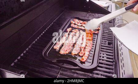 Cuisson de tranches de bacon sur un barbecue à gaz extérieur. Banque D'Images