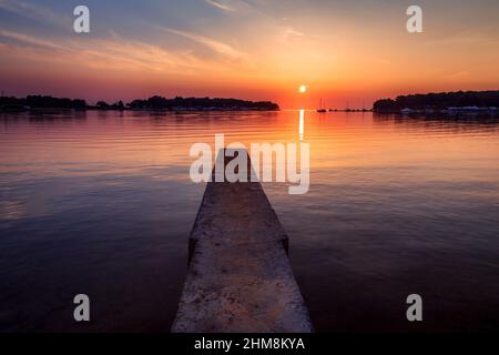 Coucher de soleil avec silhouettes de navires sur la mer Adriatique, jetée en béton au premier plan, la lagune verte à Porec - Istrie, Croatie, Europe. Banque D'Images