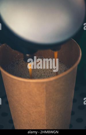 Café frais versé dans la tasse en papier de la machine à café. Mise au point sélective. Gros plan. Banque D'Images