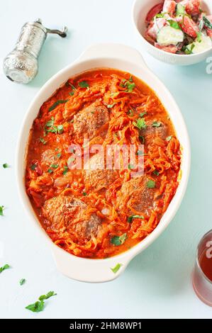 Côtelettes de viande maison avec sauce tomate dans un plat de cuisson sur fond bleu. Banque D'Images